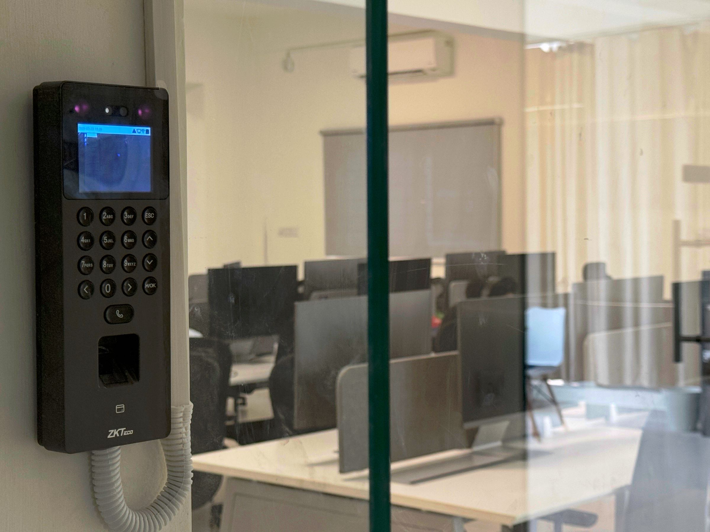 Biometric and access-card reader at the entrance to the JoinNow Bangalore office floor, workstations visible through glass.