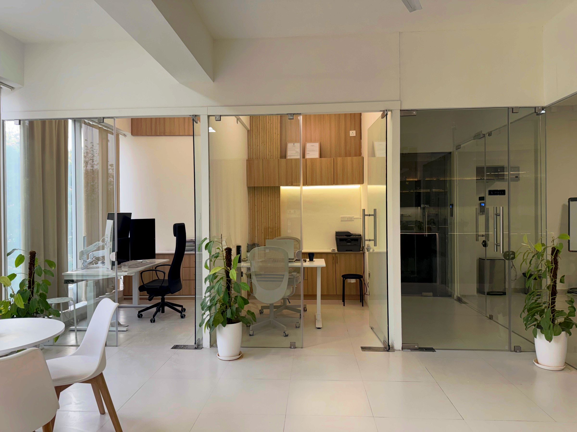 Private offices in the Bangalore office with glass partitions, dual monitors on a monitor arm and plants.